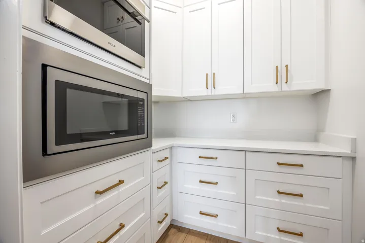 White cabinetry with gold-toned hardware, featuring built-in stainless steel appliances, solid surface countertops, and wood-finish flooring