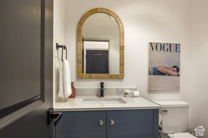Powder room featuring a blue vanity with chrome hardware, an integrated rectangular sink, a light-toned countertop, and a wood-framed arched mirror