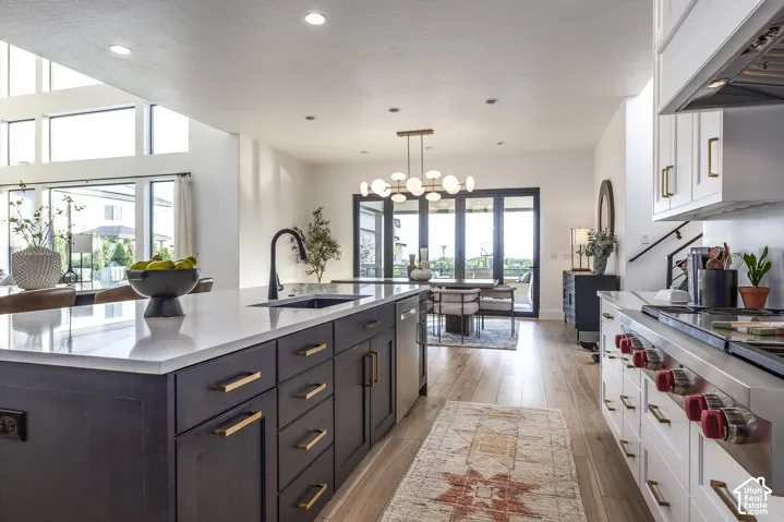 Spacious kitchen featuring a large island with a dark finish and light-toned countertop, stainless steel appliances including a professional-grade range, light wood-finish flooring, and ample cabinetry with gold-toned hardware