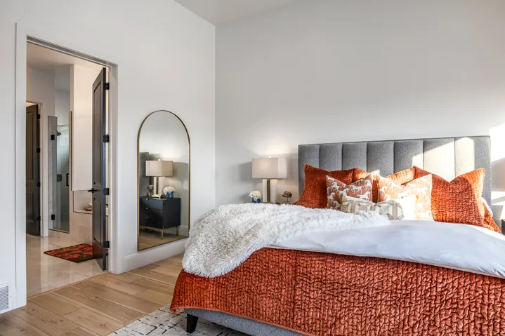 Bedroom with wood-finish flooring, a paneled upholstered headboard, and a doorway opening to a tiled bathroom