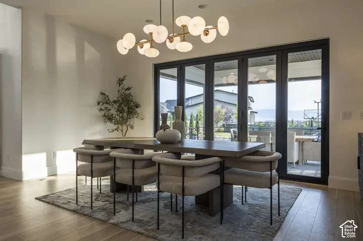 Dining area featuring a contemporary chandelier, light wood-finish flooring, and expansive multi-panel glass doors opening to an exterior patio