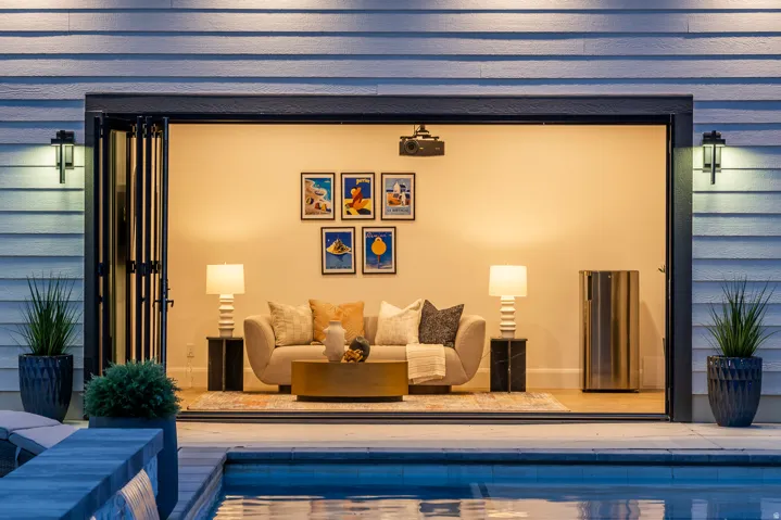 Outdoor entertaining space featuring bi-fold doors, a built-in projector, a beverage cooler, and exterior wall sconces