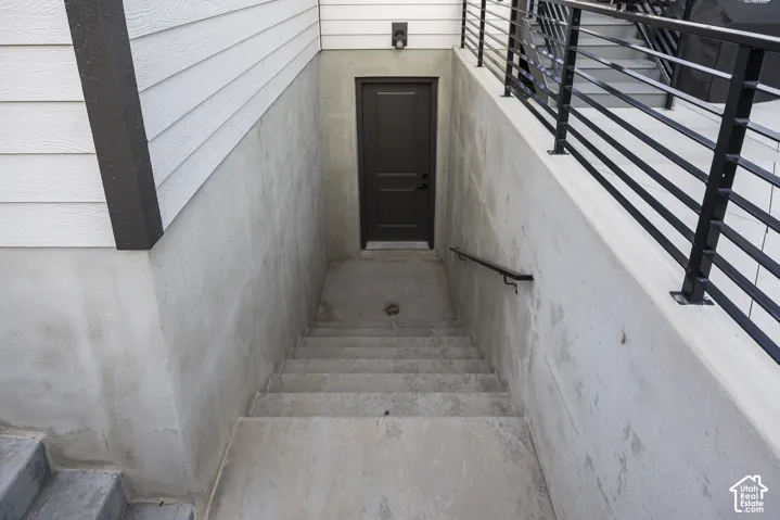 Exterior concrete staircase leading to a solid panel door, featuring a black handrail and white horizontal siding