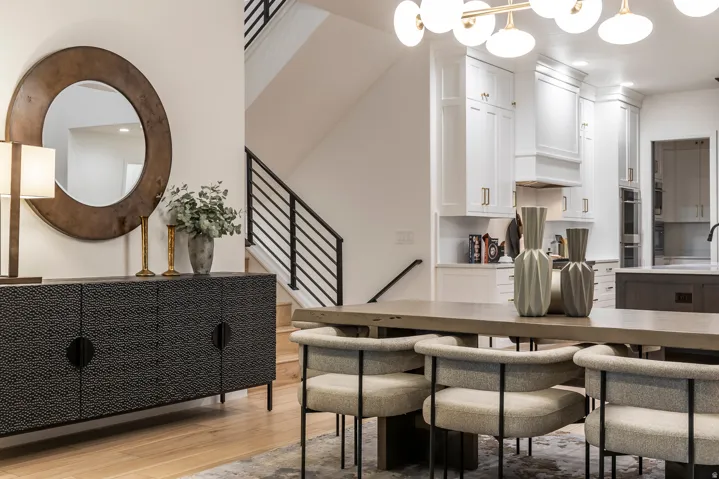 Contemporary open-concept living space featuring wood-finish flooring, a modern staircase with black metal railings, and a dining area with a linear chandelier