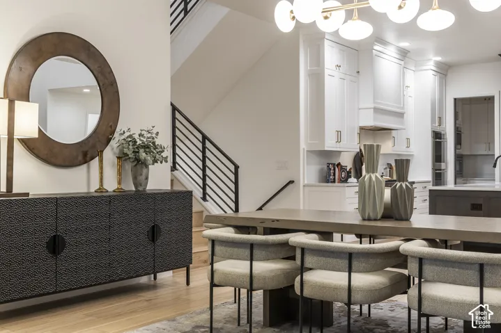 Contemporary open-concept living space featuring wood-finish flooring, a modern staircase with black metal railings, and a dining area with a linear chandelier