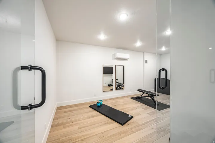 Dedicated fitness room featuring light wood-finish flooring, recessed lighting, and a glass entry door with a matte black handle