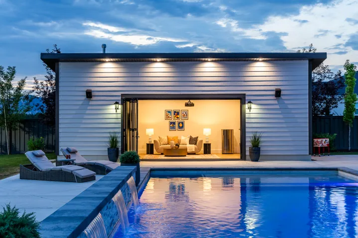 Modern pool house with wide-opening bi-fold doors, white horizontal siding, and a flat roofline