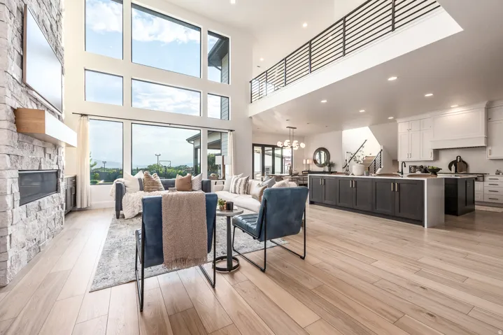 Spacious open-concept living area featuring high ceilings, a stacked stone fireplace, and light wood-finish flooring