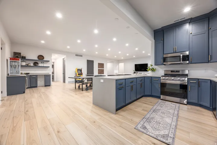 Open-concept kitchen featuring blue cabinetry, stainless steel appliances, and light wood-finish flooring