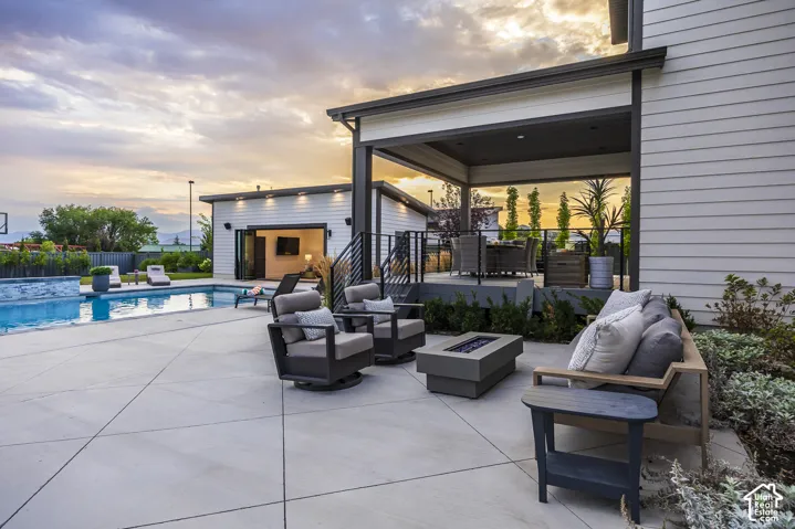 Expansive concrete patio featuring a built-in swimming pool with a stone-finish edge, a covered outdoor living area with a dark ceiling, and a separate structure with bi-fold doors