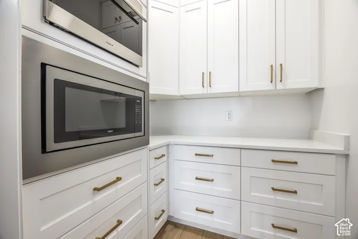 White cabinetry with gold-toned hardware, featuring built-in stainless steel appliances, solid surface countertops, and wood-finish flooring