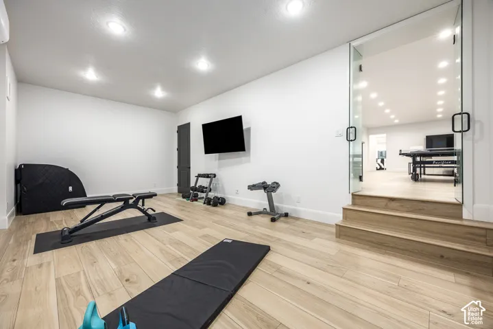Spacious room featuring light wood-finish flooring, recessed lighting, and a wall-mounted flat-screen display