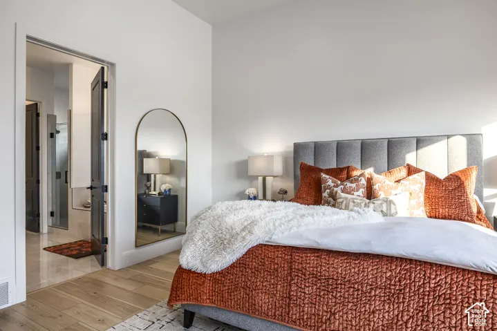 Bedroom with wood-finish flooring, a paneled upholstered headboard, and a doorway opening to a tiled bathroom