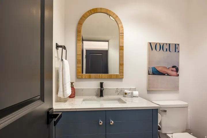 Powder room featuring a blue vanity with chrome hardware, an integrated rectangular sink, a light-toned countertop, and a wood-framed arched mirror