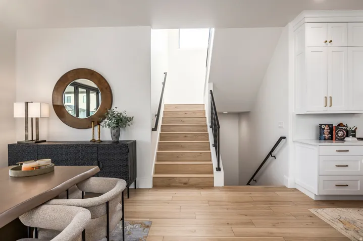 Open-concept entry area featuring light wood-finish flooring, a contemporary staircase with black railings, built-in white cabinetry, and a textured console with a round mirror