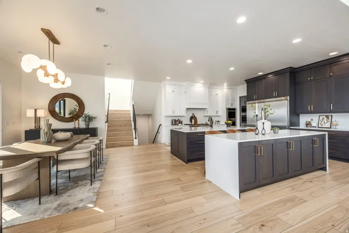 Open-concept living space featuring wood-finish flooring, a two-tone kitchen with dark lower cabinetry and white upper cabinetry, and a central kitchen island with a waterfall countertop