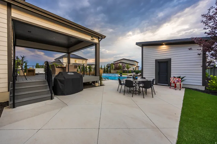 Outdoor living area featuring a spacious concrete patio, covered deck with composite decking and black railings, and an in-ground swimming pool