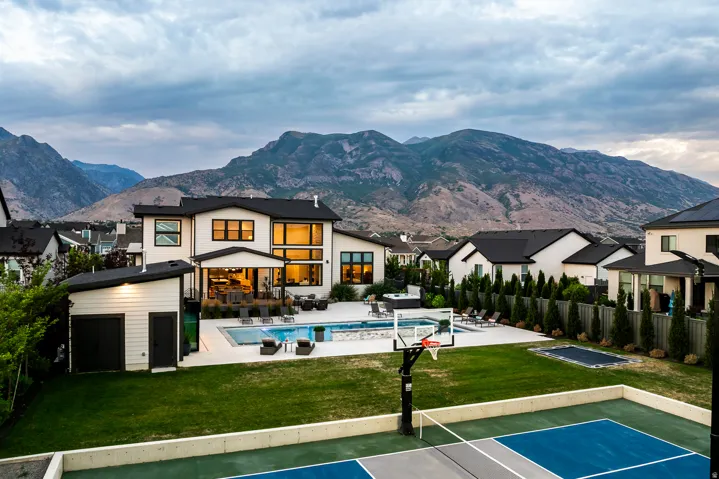 Expansive backyard featuring a multi-sport court with basketball hoop, manicured lawn, and a large swimming pool with integrated spa