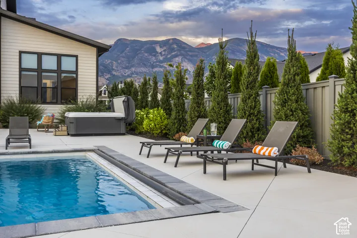 Outdoor patio featuring a rectangular swimming pool with a stone coping, an adjacent hot tub, and concrete decking
