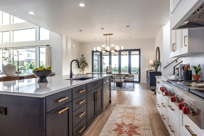 Spacious kitchen featuring a large island with a dark finish and light-toned countertop, stainless steel appliances including a professional-grade range, light wood-finish flooring, and ample cabinetry with gold-toned hardware