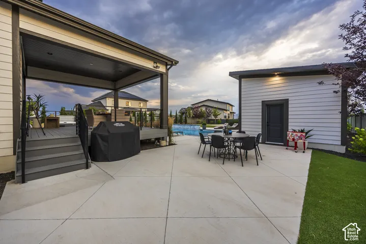 Outdoor living area featuring a spacious concrete patio, covered deck with composite decking and black railings, and an in-ground swimming pool