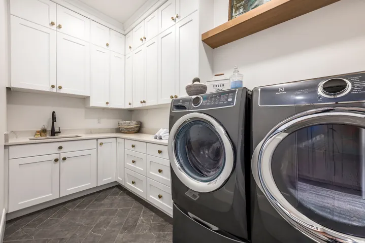 Laundry area featuring extensive white shaker cabinetry with brass hardware, light-toned countertop, and dark-toned diagonal tile flooring