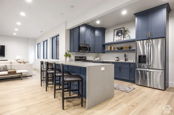 Open-concept kitchen featuring blue cabinetry, a large kitchen island with seating, stainless steel appliances, and wood-finish flooring