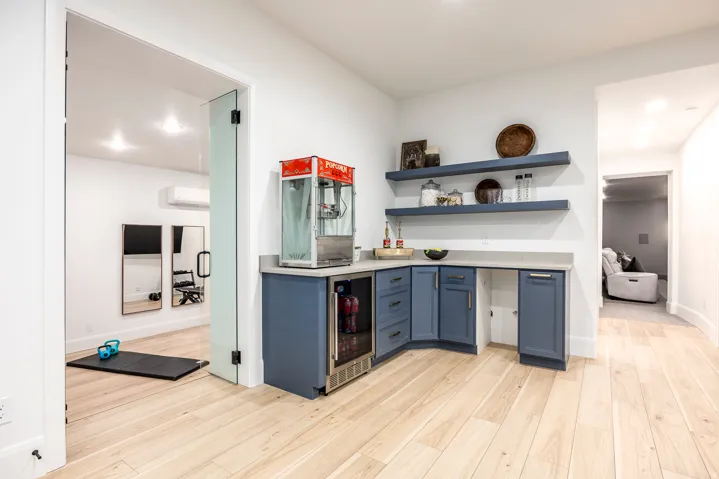 Entertainment area featuring a built-in wet bar with blue cabinetry, light-toned countertop, and floating shelves