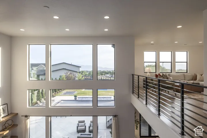 Two-story living area featuring a grid of large windows, a second-story open hallway with a horizontal slat railing, and recessed ceiling lighting