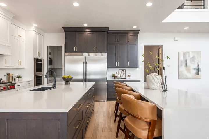 Gourmet kitchen featuring a large central island with an undermount sink, light-toned countertops, two-tone cabinetry, stainless steel appliances, and wood-finish flooring