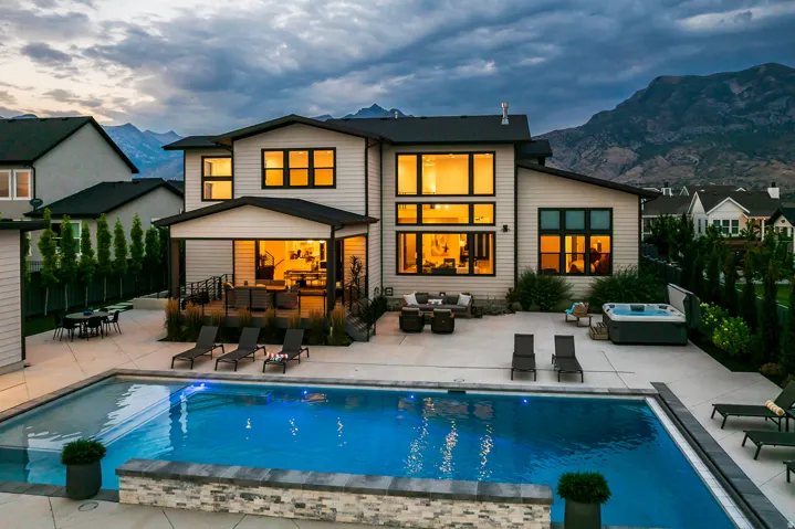 Expansive backyard featuring a rectangular swimming pool with stone-clad retaining wall, a built-in spa, a covered patio, and a large concrete patio area