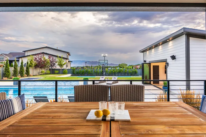 Expansive outdoor living area featuring a wooden patio table, glass panel railing, and a swimming pool