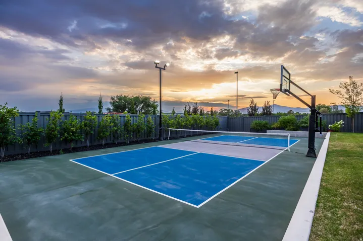 Multi-sport court featuring a pickleball setup with a net, basketball hoop, and perimeter lighting