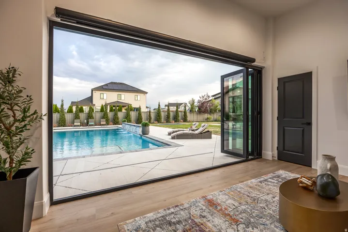 Expansive bi-fold glass doors open to a backyard featuring a swimming pool with a waterfall element, a surrounding patio, and mature landscaping