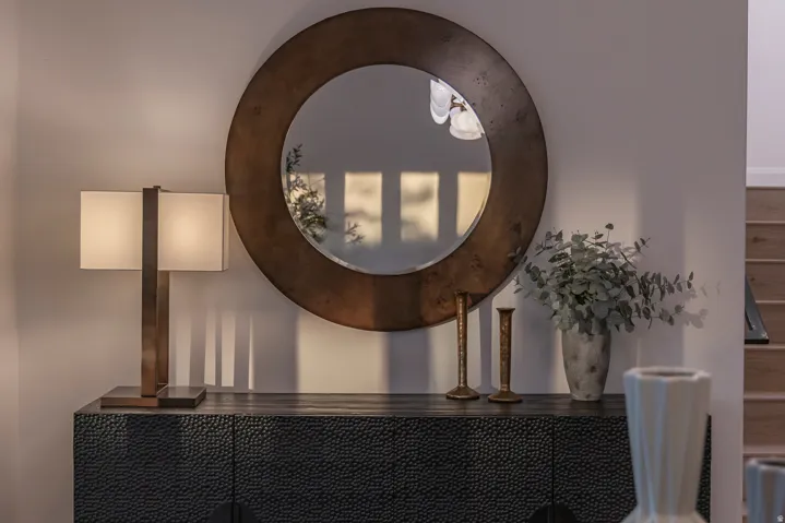 Textured black console cabinet beneath a large circular mirror with a bronze-toned frame