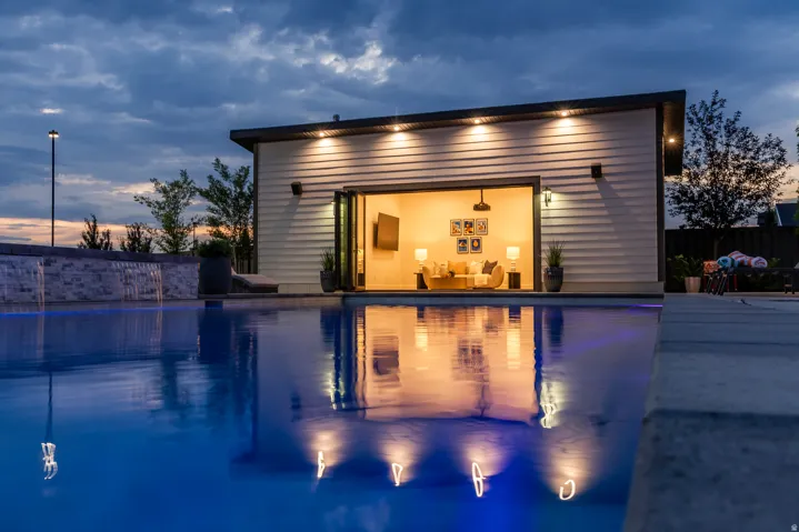 Expansive swimming pool featuring an integrated waterfall and an illuminated pool house