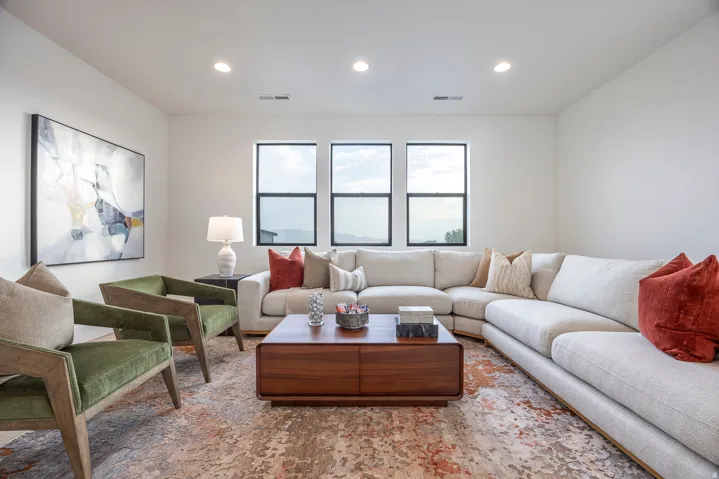Spacious living area featuring three square windows with black frames, recessed ceiling lighting, a contemporary area rug, and light-toned walls