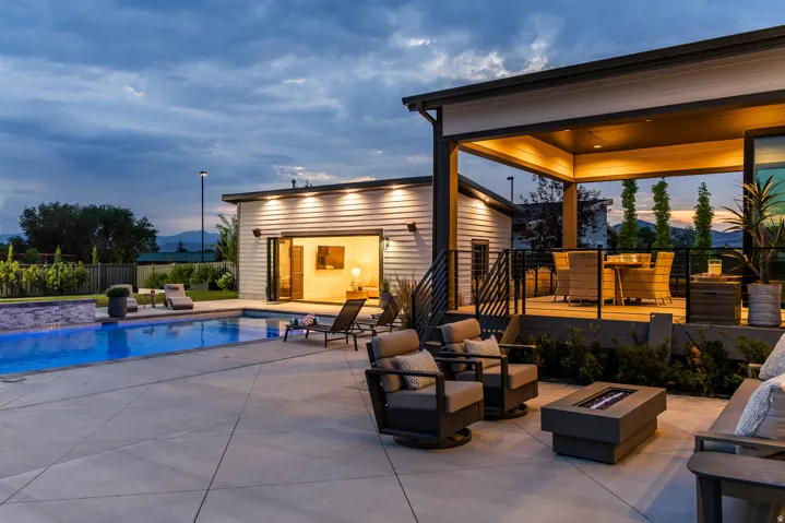 Expansive outdoor living area featuring a swimming pool, concrete patio, covered deck, and a detached structure with accordion doors