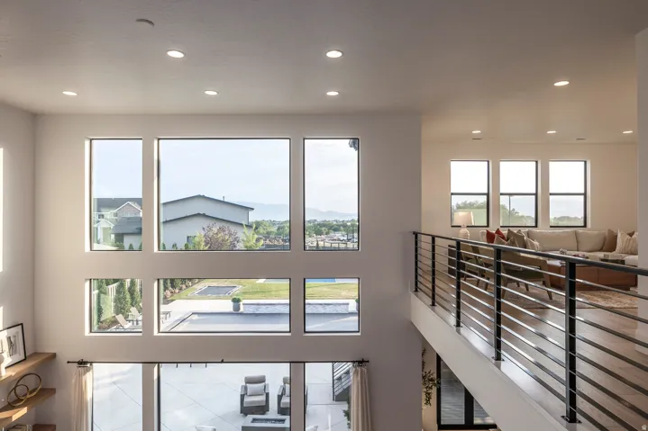 Two-story living area featuring a grid of large windows, a second-story open hallway with a horizontal slat railing, and recessed ceiling lighting