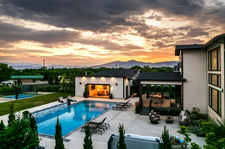 Expansive exterior featuring a large swimming pool, a covered outdoor deck, an additional building with bi-fold doors, a hot tub, and a sports court