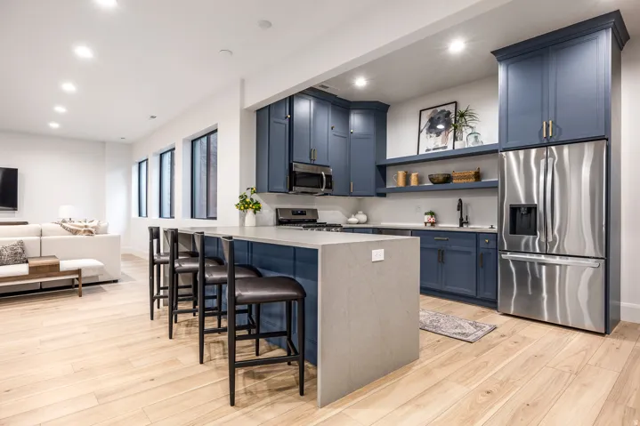 Open-concept kitchen featuring blue cabinetry, a large kitchen island with seating, stainless steel appliances, and wood-finish flooring