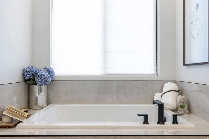 Built-in soaking tub featuring matte black fixtures, set into a light-toned countertop, and surrounded by large-format gray tiled walls