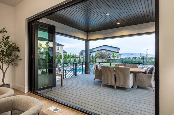 Expansive covered patio featuring a wide-plank deck, recessed lighting, and a black metal railing overlooking a swimming pool