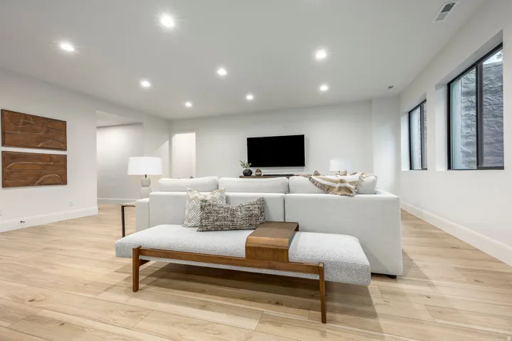 Spacious living area featuring light wood-finish flooring, recessed lighting, and bright white walls