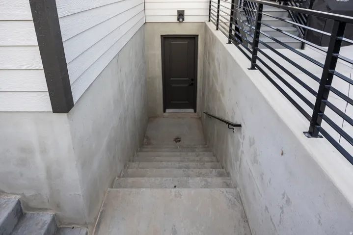 Exterior concrete staircase leading to a solid panel door, featuring a black handrail and white horizontal siding
