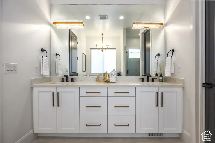 Double vanity featuring white cabinetry with gold-finish hardware, a light-toned countertop, and dual black-finish faucets