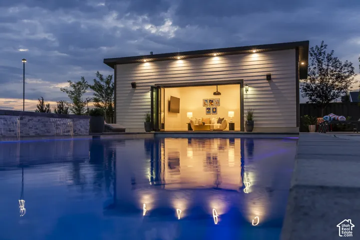 Expansive swimming pool featuring an integrated waterfall and an illuminated pool house