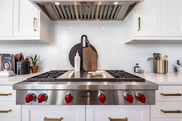 Stainless steel range with red control knobs, framed by white cabinetry with brass hardware