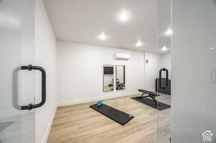 Dedicated fitness room featuring light wood-finish flooring, recessed lighting, and a glass entry door with a matte black handle