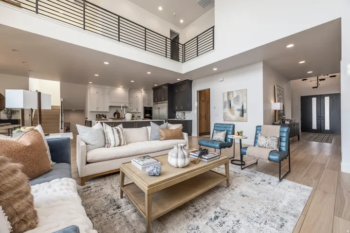 Open-concept living area featuring high ceilings, wood-finish flooring, and a second-story interior balcony with black metal railing